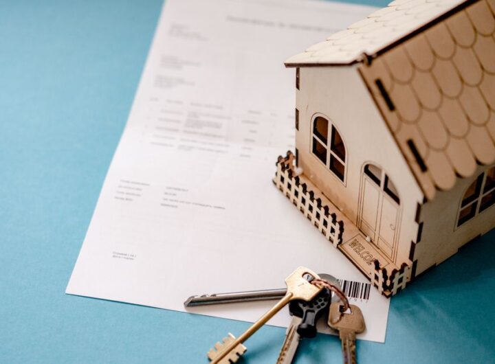 Miniature wooden house with keys and contract symbolizing real estate transactions.