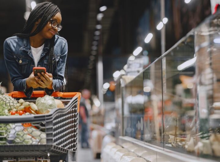 A young woman with afro braids grocery shopping in a supermarket, using a mobile phone.