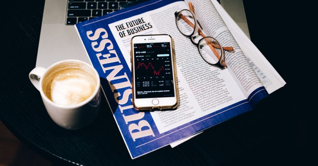 A business setup with a laptop, coffee, phone, and newspaper. Perfect for finance themes.