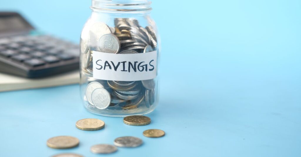 Glass jar labeled 'Savings' filled with coins, beside a calculator on a blue background.