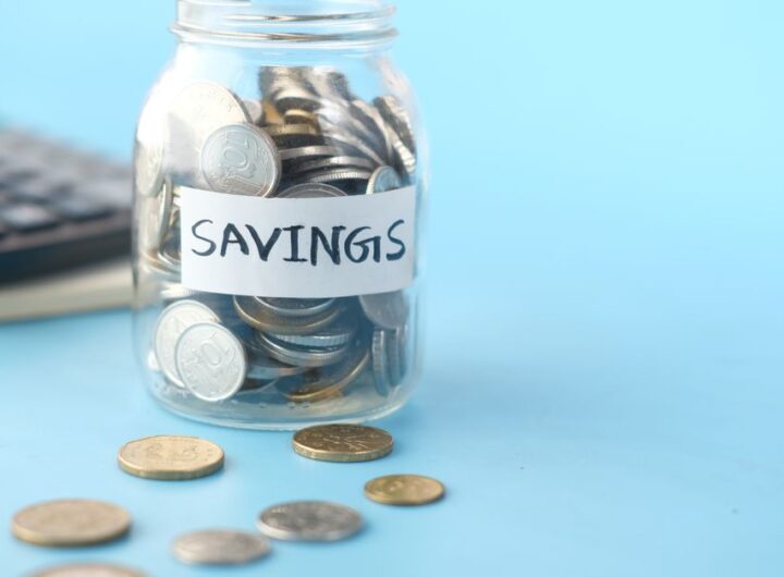 Glass jar labeled 'Savings' filled with coins, beside a calculator on a blue background.